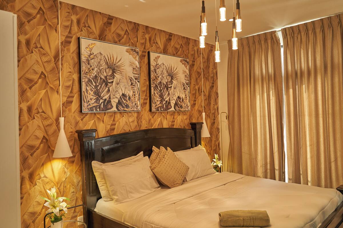 A neatly made bed with a wooden headboard, two wall-mounted paintings, and a bedside lamp.