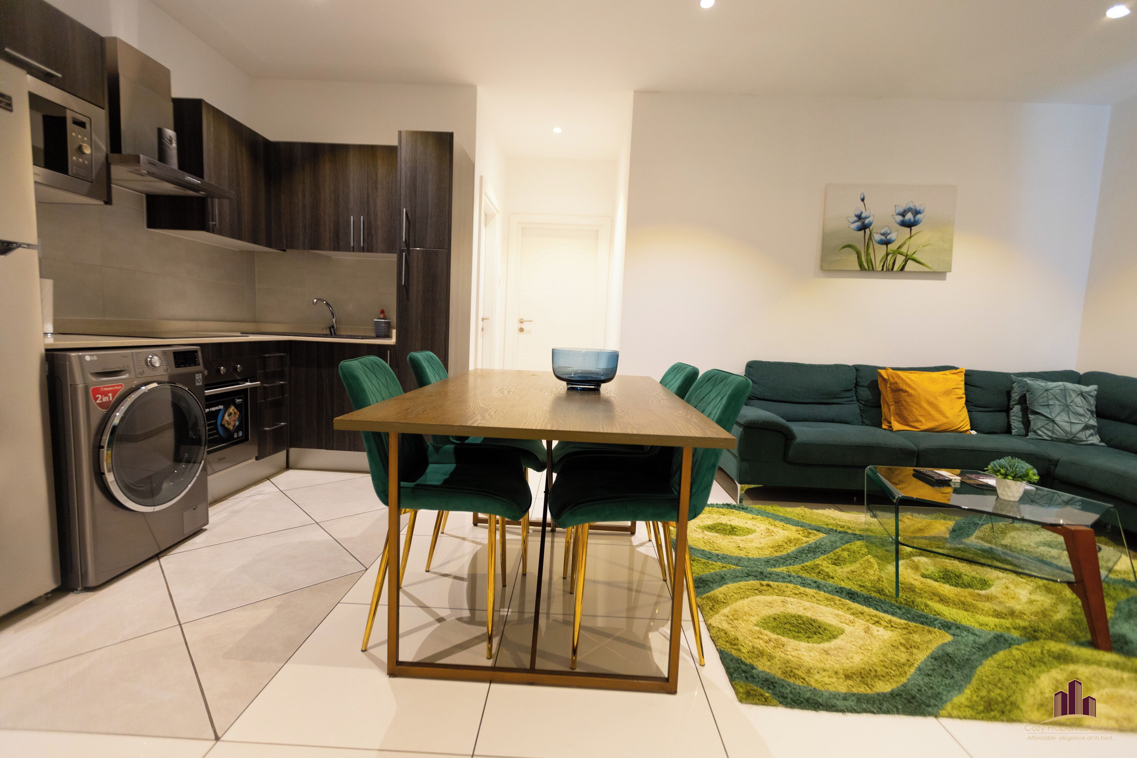 Una cocina moderna con lavadora integrada, un comedor con mesa y sillas, y una sala de estar con sofá y mesa de centro.