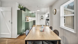 A dining area with a wooden table, chairs, a potted plant, and a kitchen in the background.