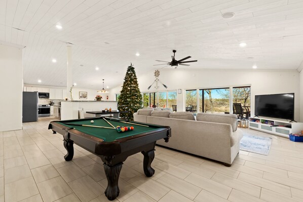 Un vaste salon avec une table de billard, un grand sapin de Noël et, au fond, une cuisine moderne.