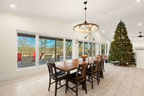 Un vaste espace dédié à la salle à manger, avec une grande table et des chaises en bois, un lustre moderne et un sapin de Noël décoré.