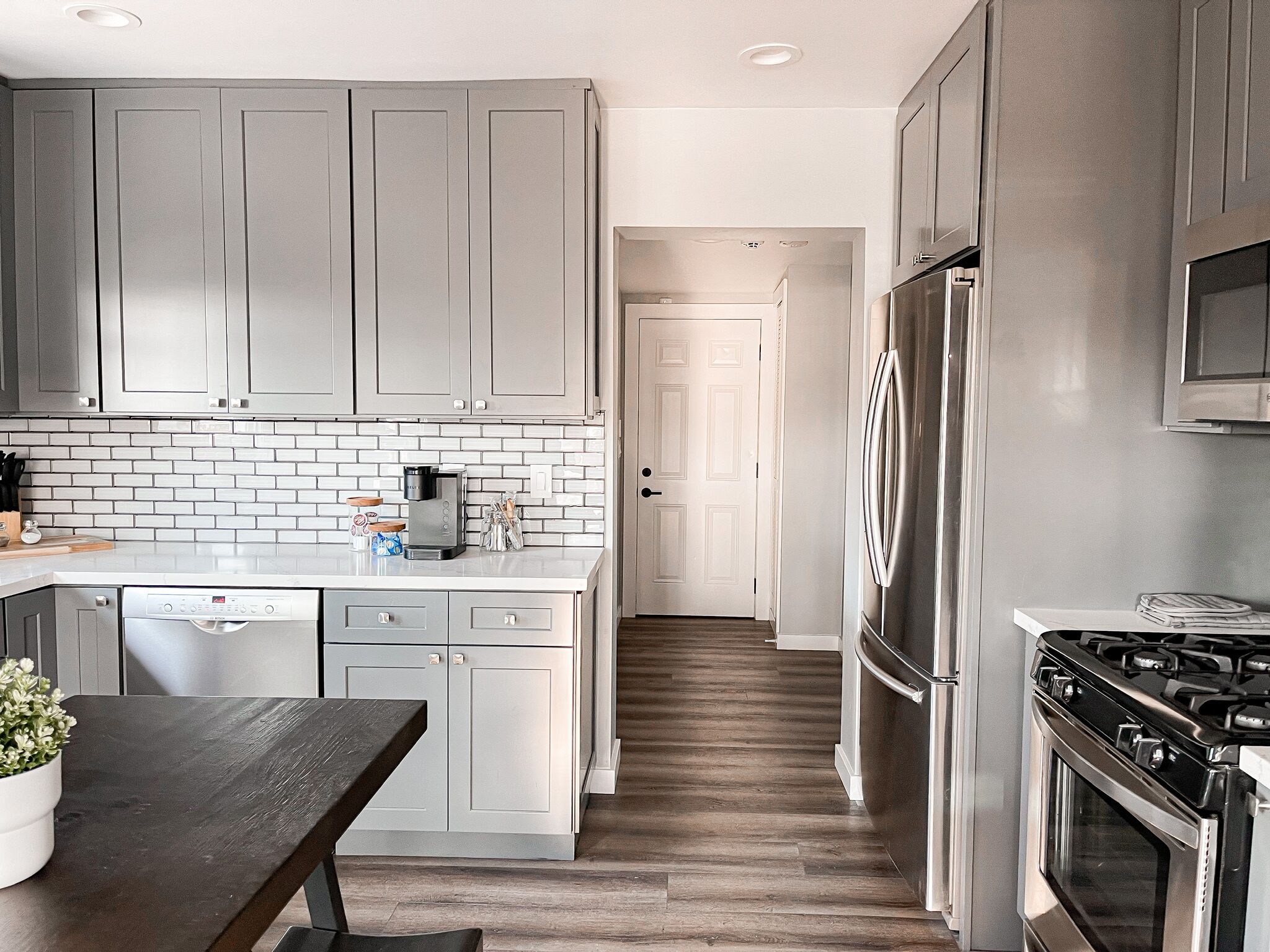 A modern kitchen with grey cabinets, a white tiled backsplash, a stainless steel refrigerator, and a black stove.
