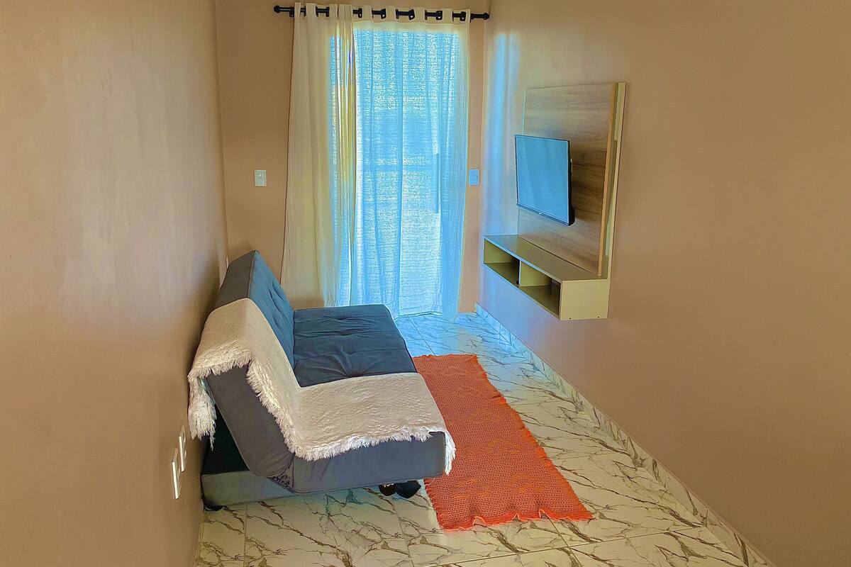 A bedroom with a bed, a TV mounted on the wall, and a window with curtains.
