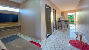 Quarto de hotel moderno com uma cama grande, televisão, pequena área de cozinha e vista para o verde lá fora.