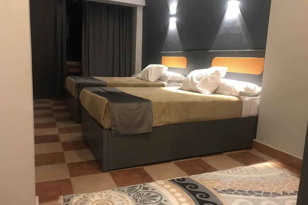 A hotel room with a checkered floor, a bed with a headboard, and a patterned rug.