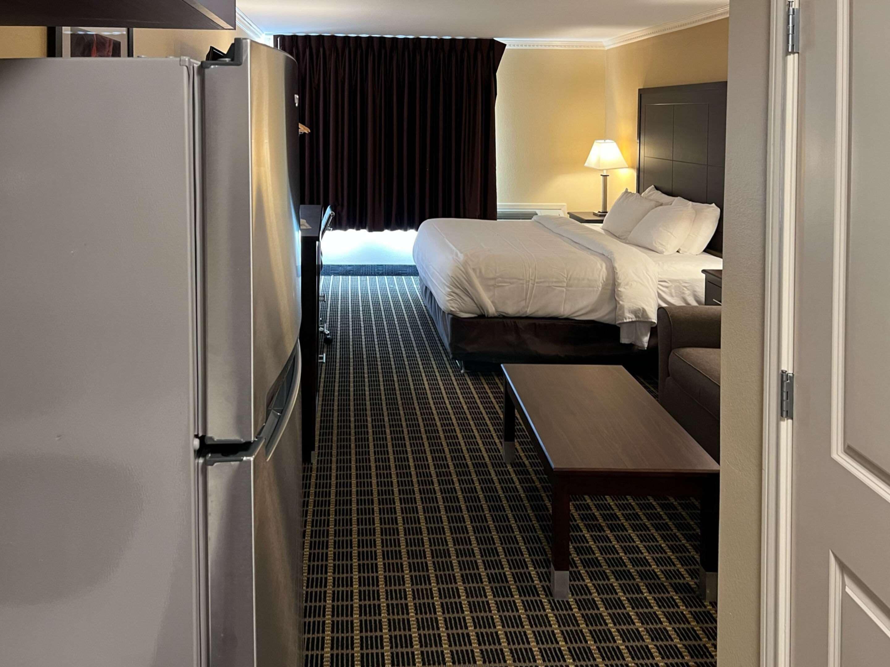 A hotel room with a bed, a desk, a chair, a lamp, and a refrigerator.