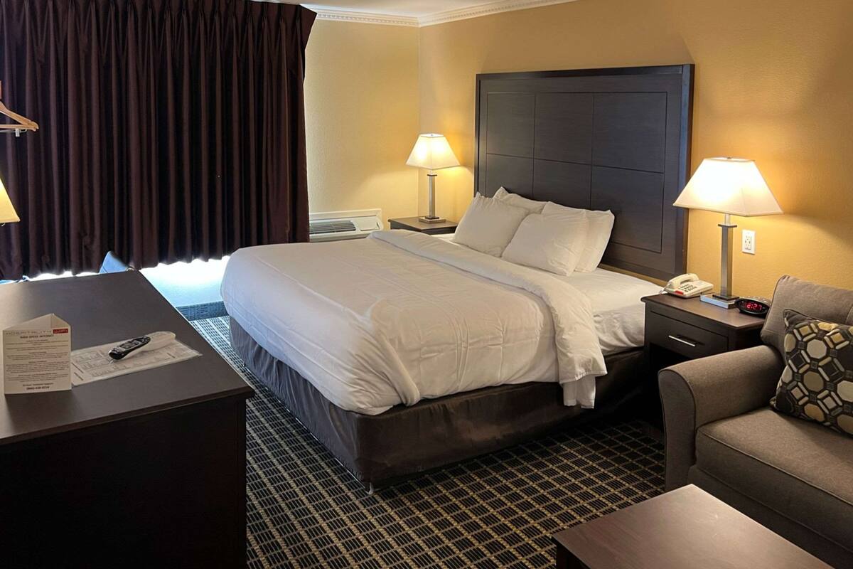 Une chambre d’hôtel avec un grand lit, deux tables de chevet avec des lampes, un canapé et un bureau avec un téléphone et des documents.