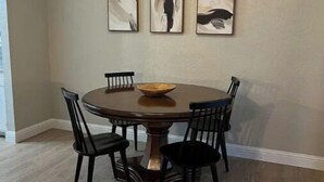 Uma sala de jantar com uma mesa redonda, seis cadeiras e três quadros abstratos na parede.