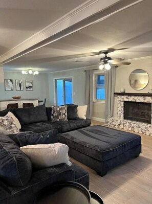 Relax in a cozy seating area with a fireplace, sectional sofa, and ottoman, surrounded by artwork and a view of the outdoors.