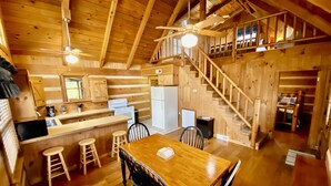 A wooden cabin interior with a dining area, kitchen, and a staircase leading to an upper level. - Log Cabin, walk to National park trails and minutes from Gatlinburg with a view! (Townsend)