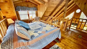 A cozy attic bedroom with a large bed, wooden beams, a window with blinds, and a chair. - Log Cabin, walk to National park trails and minutes from Gatlinburg with a view! (Townsend)