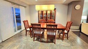 Un comedor con mesa y sillas de madera, una araña y un reloj en la pared.
