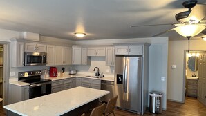 A modern kitchen with stainless steel appliances, a marble countertop island, and wooden flooring. - Top Floor Lakefront Condo with Mountain Views! (Wasilla)