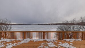 A wooden deck with snow on the ground and a frozen lake in the background. - Top Floor Lakefront Condo with Mountain Views! (Wasilla)