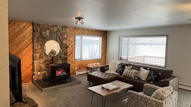 A cozy living room with a stone wall, a fireplace, a brown leather sofa, a patterned armchair, and a coffee table. - Top Floor Lakefront Condo with Mountain Views! (Wasilla)