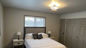 A bedroom with a bed, two bedside tables with lamps, a window with blinds, a ceiling light fixture, and a set of closets. - Top Floor Lakefront Condo with Mountain Views! (Wasilla)