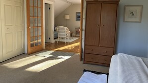 Een slaapkamer met een houten garderobe, een bed met een witte dekbedovertrek, een witte stoel en een houten vloer.