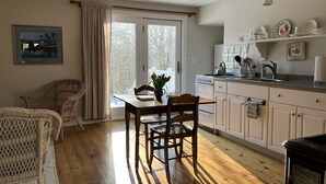 Een gezellige keuken met houten vloeren, een eettafel met stoelen, een raam met gordijnen en een keukentrap met diverse spullen.
