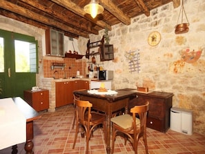 A rustic kitchen with a wooden table, chairs, and a stone wall.