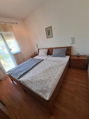 Un dormitorio con cama, cabecera de madera, mesitas de noche y una ventana con cortinas.