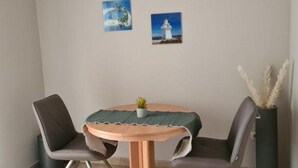 Ein kleiner Essbereich mit einem runden Tisch, zwei Stühlen, einer Zimmerpflanze und zwei gerahmten Bildern an der Wand.