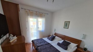 Ein Doppelbett mit Holz Kopfteil, ein Nachttisch mit Lampe und ein Fenster mit Vorhängen.