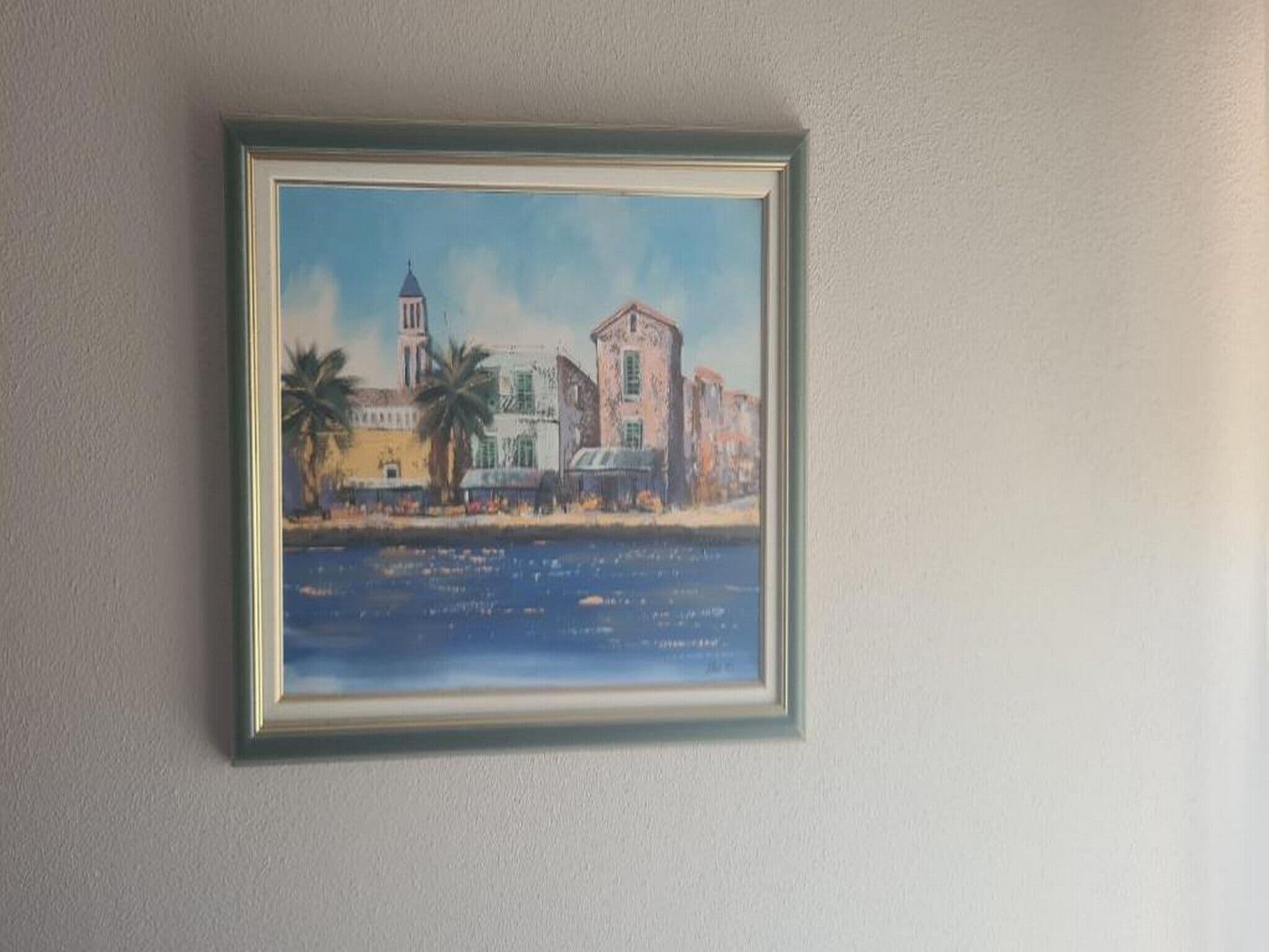 A framed painting of a coastal scene with buildings and palm trees.