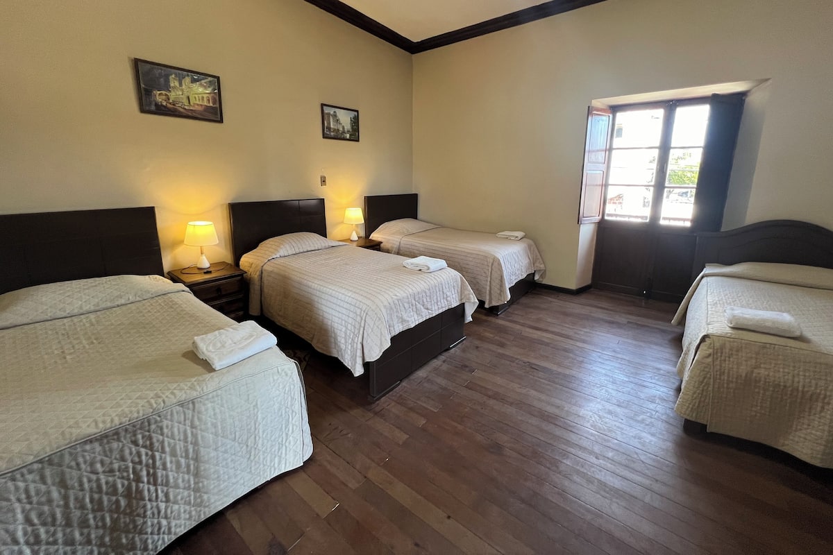 A hotel room with three beds, wooden flooring, and two wall-mounted lamps.