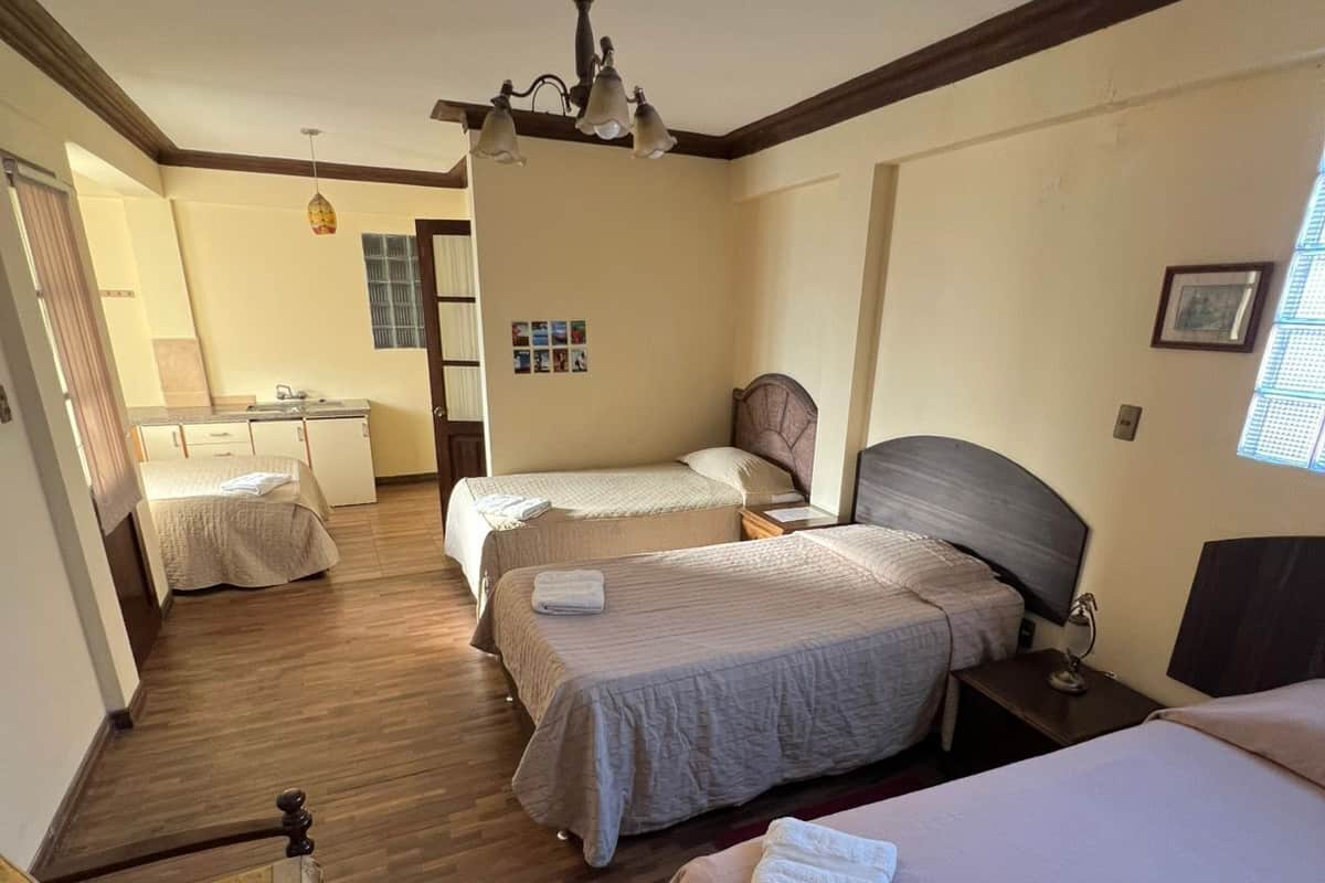 A hotel room with two beds, a wooden floor, a kitchenette, and a ceiling fan.