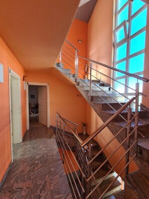 Un escalier avec des rampes en métal menant à un palier, une porte à gauche et une grande fenêtre à droite.