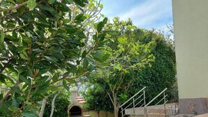 Un espace extérieur aménagé en patio, avec une table et des chaises en pierre, un petit arbre et un escalier menant à une zone abritée.