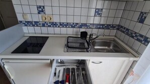 Une cuisine compacte équipée d’une cuisinière intégrée, d’un évier et d’un tiroir contenant des ustensiles.