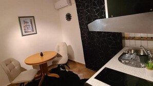 Kompakti keittiö, jossa on musta välitila, pieni ruokapöytä ja yksi tuoli.