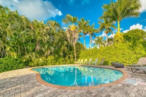 A swimming pool with a brick border, surrounded by lush greenery and palm trees. - The Palms House Miami (Miami)
