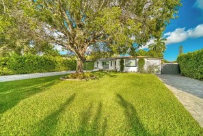 A house with a well-maintained lawn, a large tree in front, and a paved driveway. - The Palms House Miami (Miami)