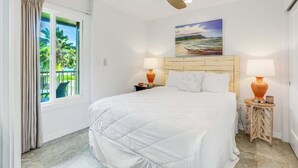 Une chambre à coucher avec un lit, deux tables de chevet avec des lampes, un ventilateur de plafond, une fenêtre avec des rideaux et un tableau au mur.
