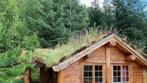 Une cabane en bois avec un toit de chaume, des marches en pierre menant à l’entrée et une petite terrasse avec des chaises.