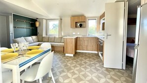 Une cuisine compacte avec des meubles en bois, un coin repas avec une table et des chaises blanches, et un canapé avec des coussins.