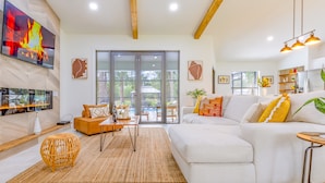 Una sala de estar moderna con un sofá blanco, un televisor montado en la pared y un ventanal con vistas al exterior.