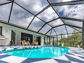 Un espace piscine doté d’une structure de plafond aux formes géométriques, d’un coin salon extérieur et d’une vue sur les palmiers.