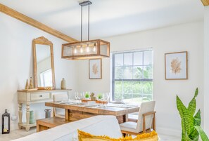 Une pièce bien éclairée, avec une table à manger en bois, des chaises, un grand miroir et un luminaire suspendu.