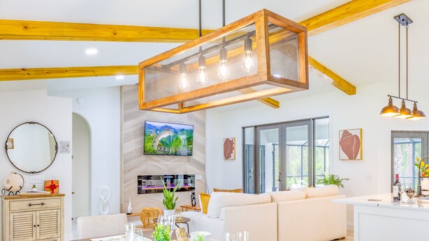 Una sala de estar moderna con techo de madera, un comedor con mesa de madera dispuesta para cuatro personas, y un sofá al fondo.