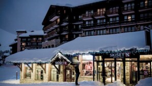Un hotel con una tienda de esquí llamada 'SKISSET' y una persona de pie frente a él.
