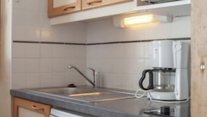 Una cocina con gabinetes blancos, un lavamanos de acero inoxidable, una cafetera y un lavavajillas.