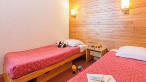 Una habitación pequeña y acogedora con dos camas individuales, cabecero de madera y dos luces de pared.
