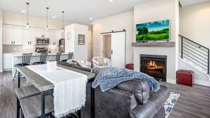 Una sala moderna con chimenea, un comedor con una mesa grande y una cocina con armarios blancos.