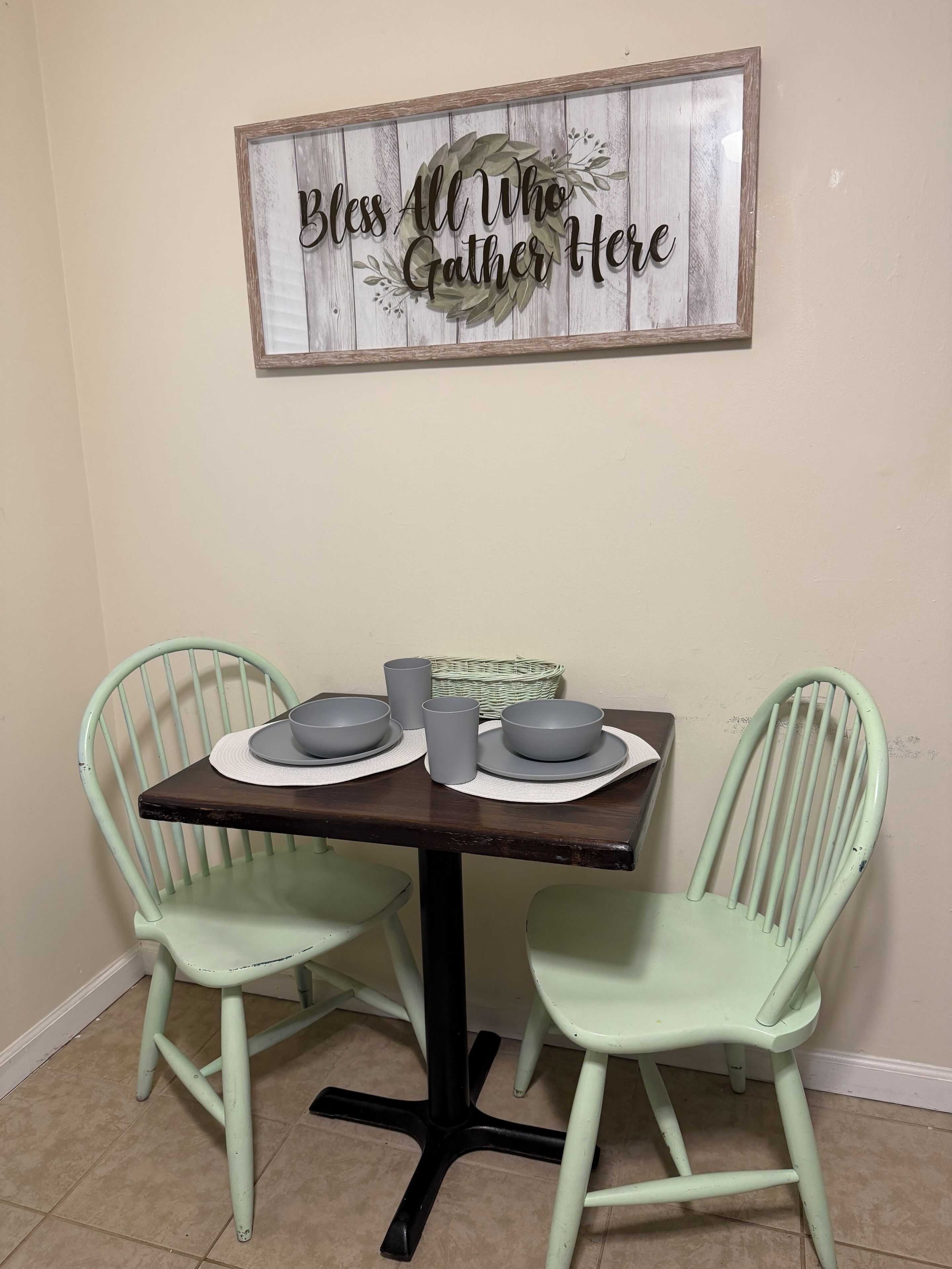 Uma mesa de jantar com duas cadeiras, uma placa na parede e uma cesta.