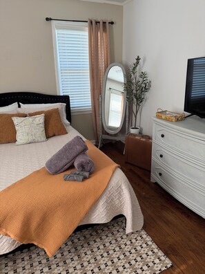A neatly arranged bedroom with a bed, a dresser, a mirror, and a television.