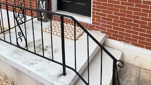 Un edificio de ladrillo con una puerta negra, un cartel de bienvenida y un felpudo.