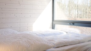 A bedroom with a large window, wooden walls, and a bed with white bedding.